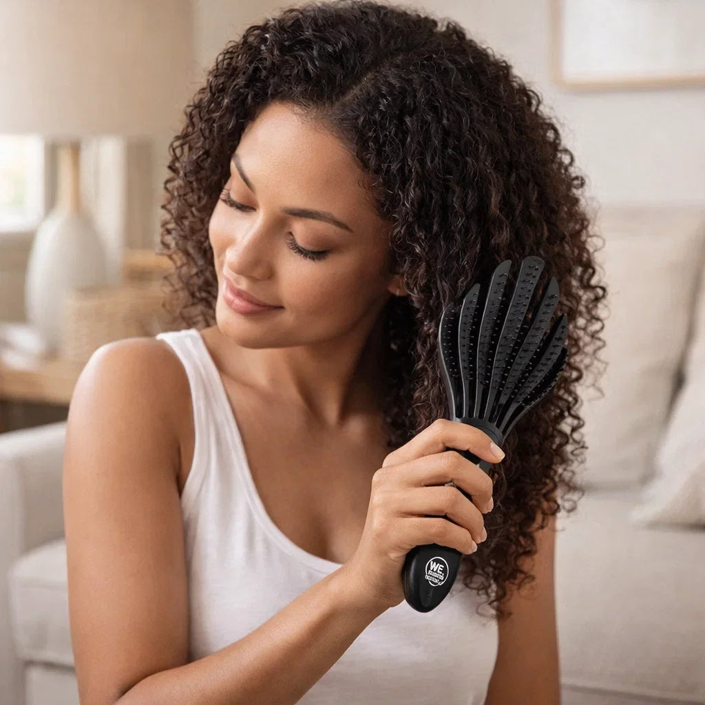 Curly-haired woman brushing hair with a black HairCare detangling brush.